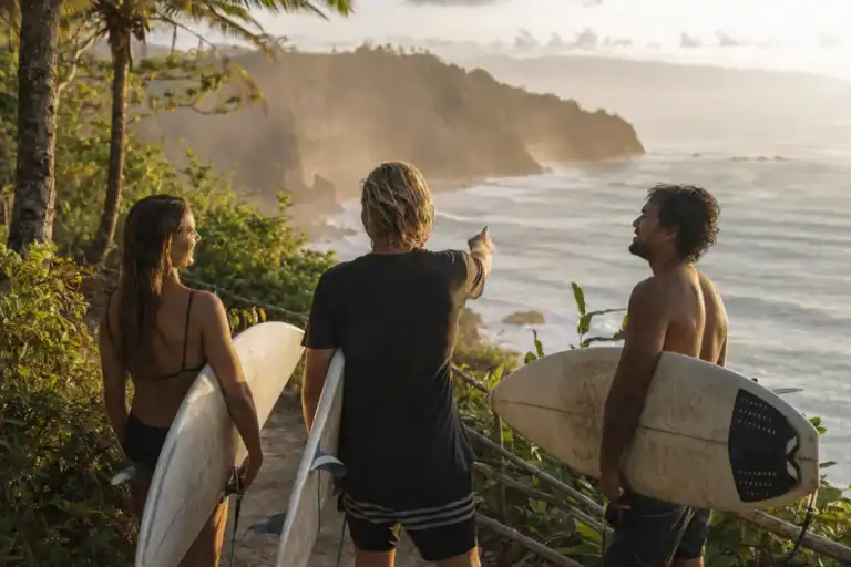 Three surfers checking a tropical coastline from a cliff trail